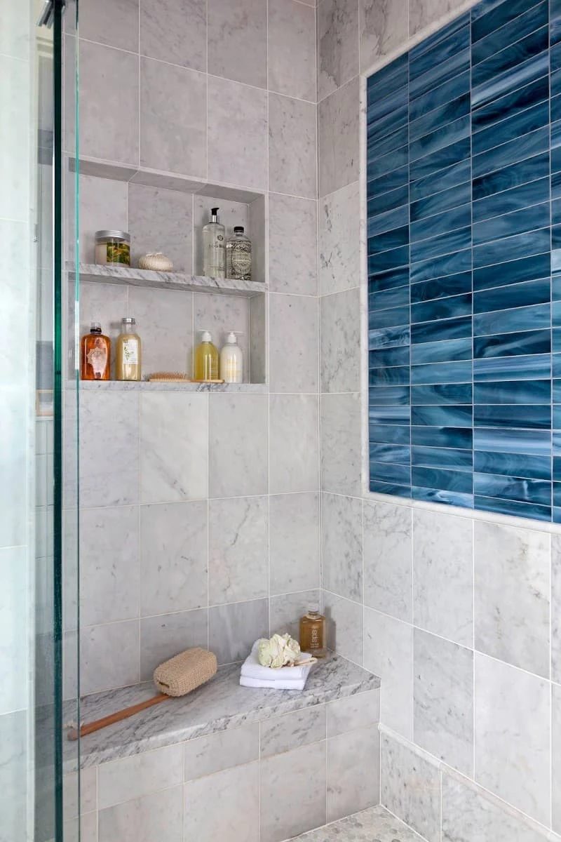 Deep blue rectangular shower tiles forming an accent panel beside pale marble-look tiles