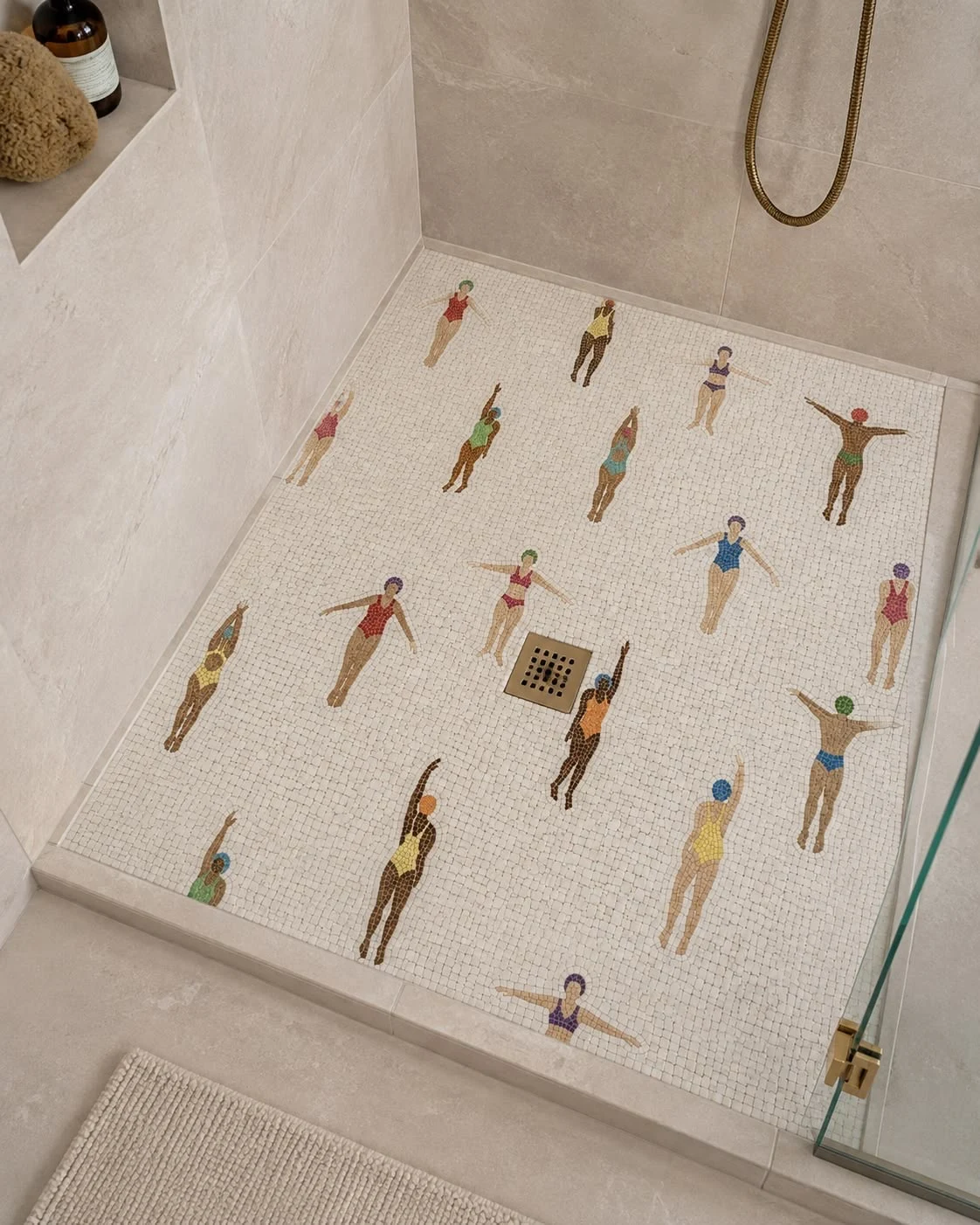 Pale mosaic shower floor decorated with colourful swimmer figures, surrounded by neutral stone-look walls