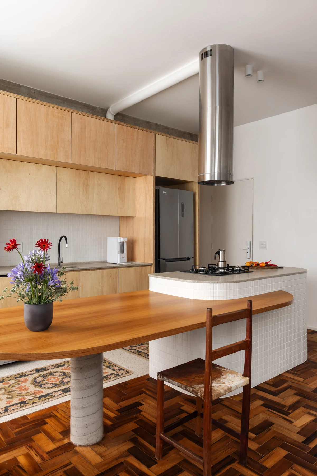 Kitchen peninsula with cooktop, cylindrical extractor and timber dining surface beside it