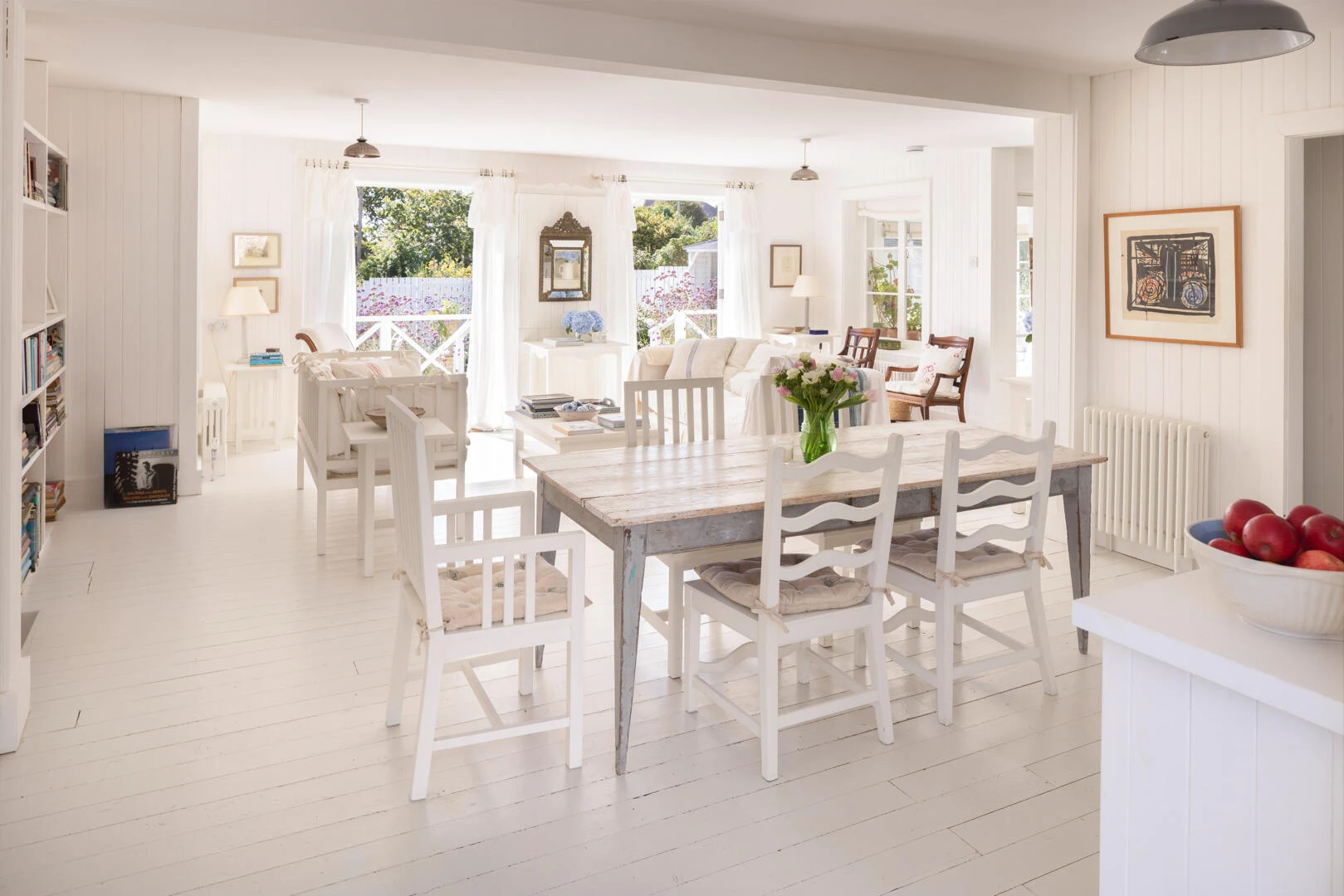 White dining chairs, pale table and kitchen beyond