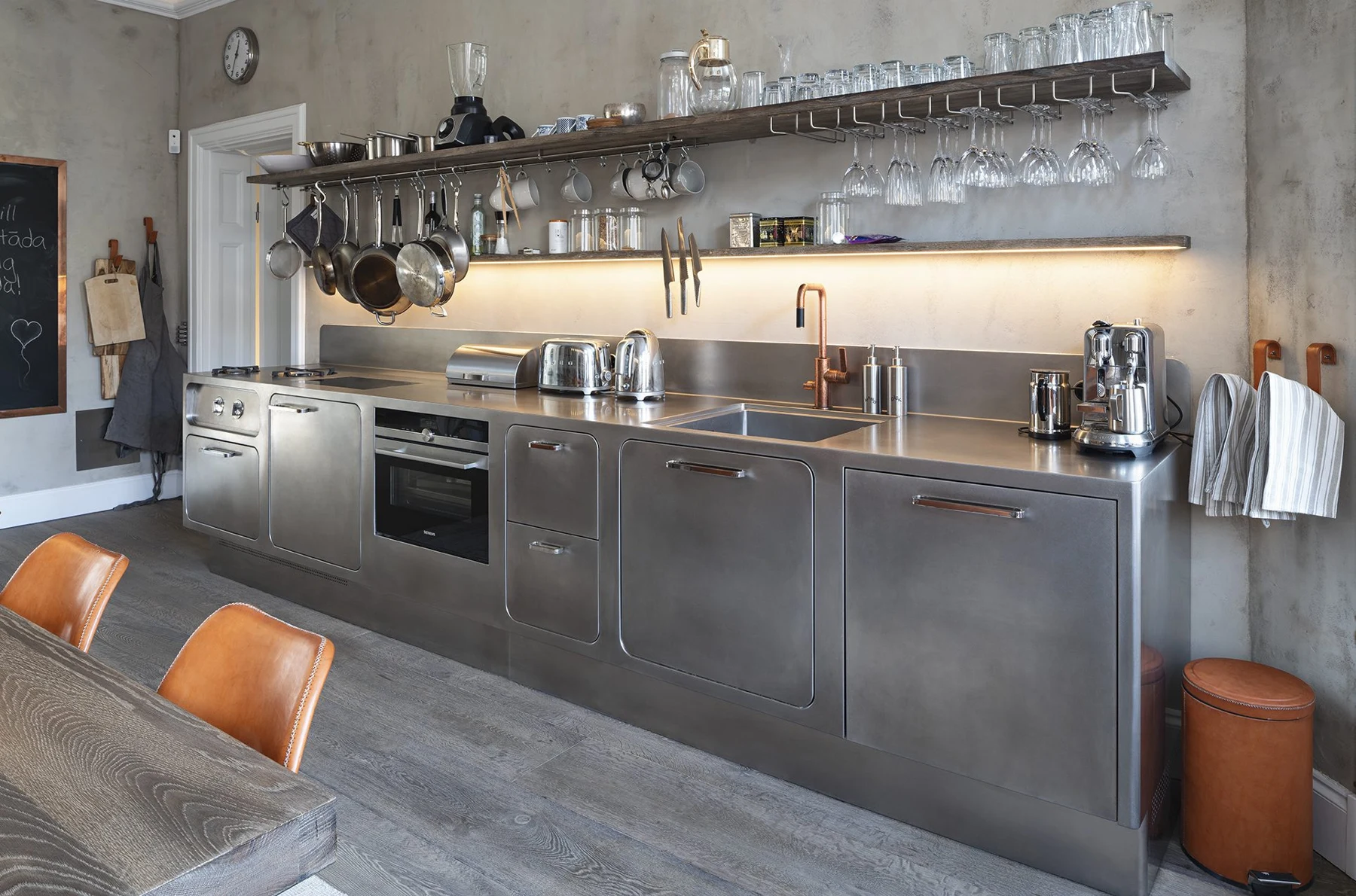 Stainless-steel kitchen with open timber shelves and pans, utensils and glasses hanging above the worktop