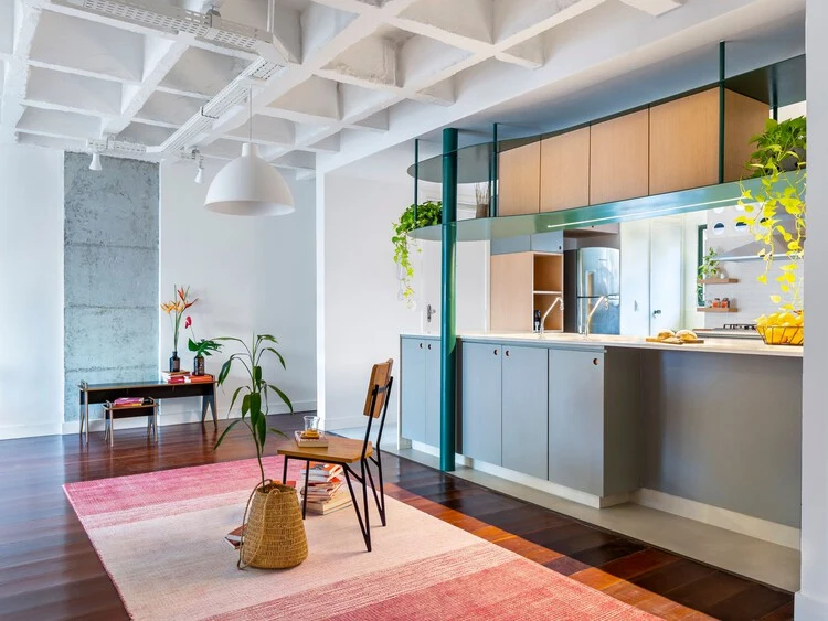 Kitchen opening into the living room beneath a white exposed ceiling grid and ceiling-mounted lamps