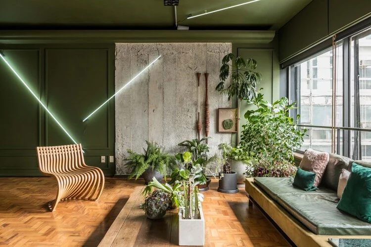 Living room with a tall raw concrete wall section contrasting with green painted walls, beside plants and timber furniture
