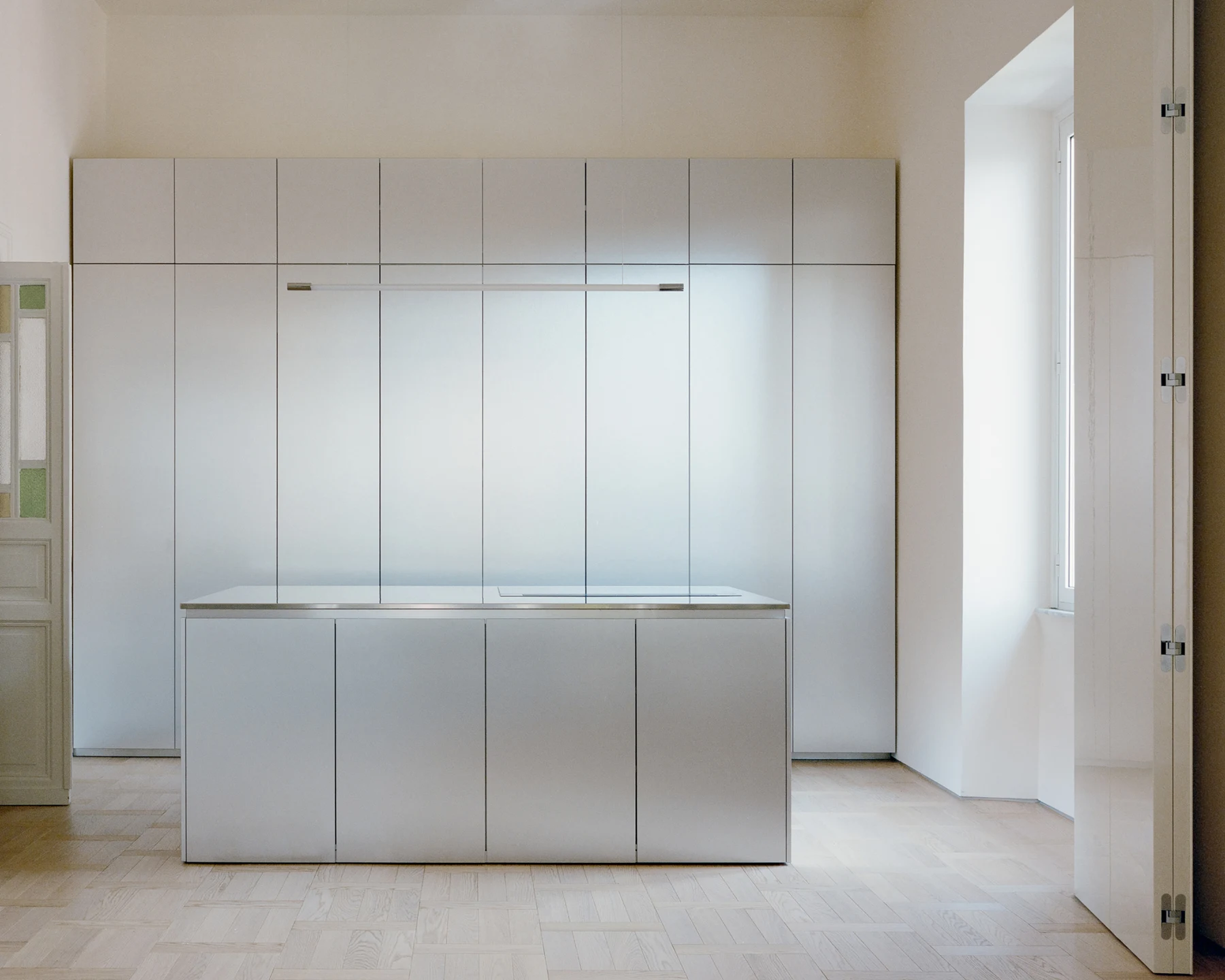 Reflective stainless-steel kitchen island in front of a continuous wall of closed panels