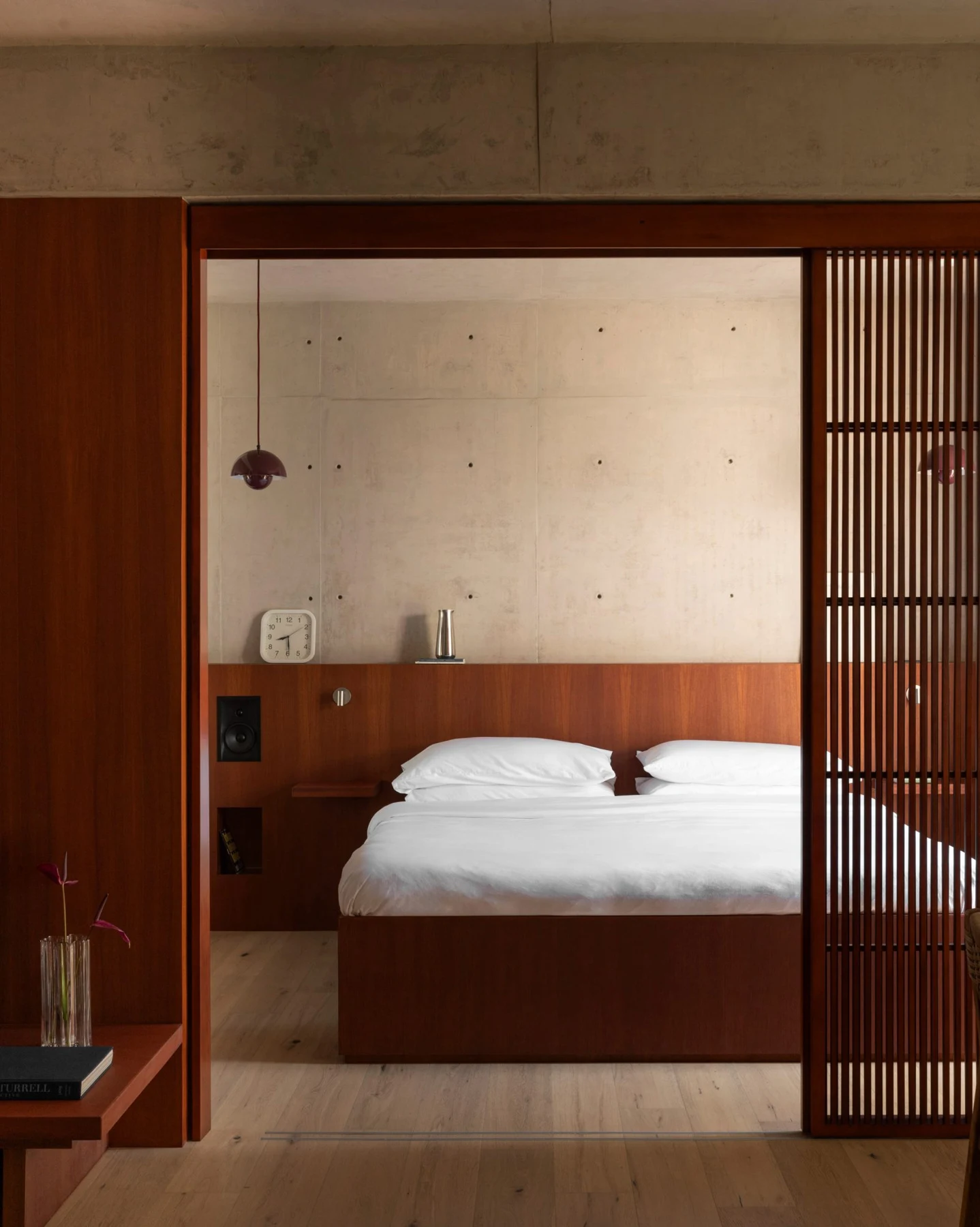 Bedroom with timber bed, full-width headboard, concrete wall and wood flooring