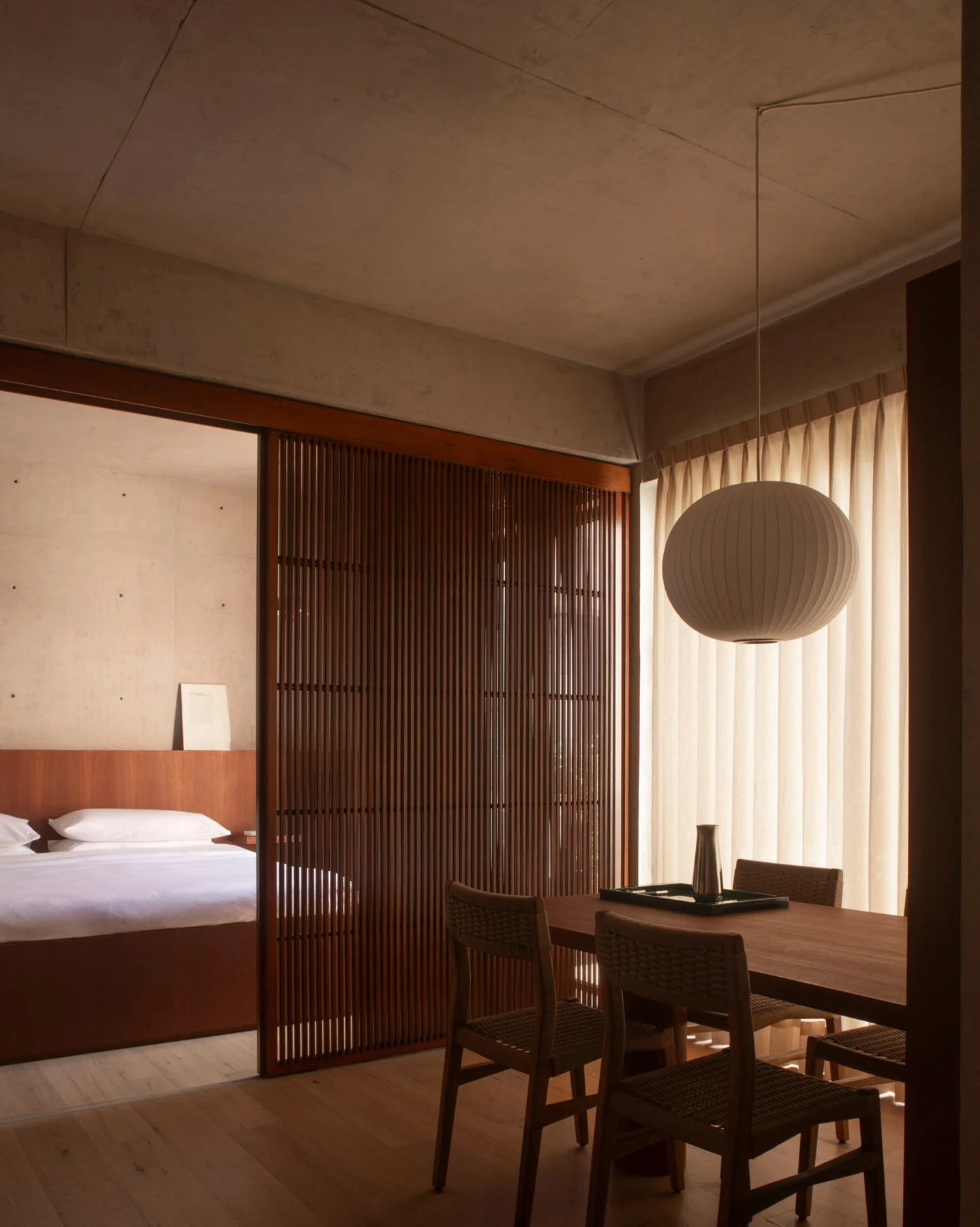 Bedroom and dining area joined by oak flooring, with a sliding timber screen