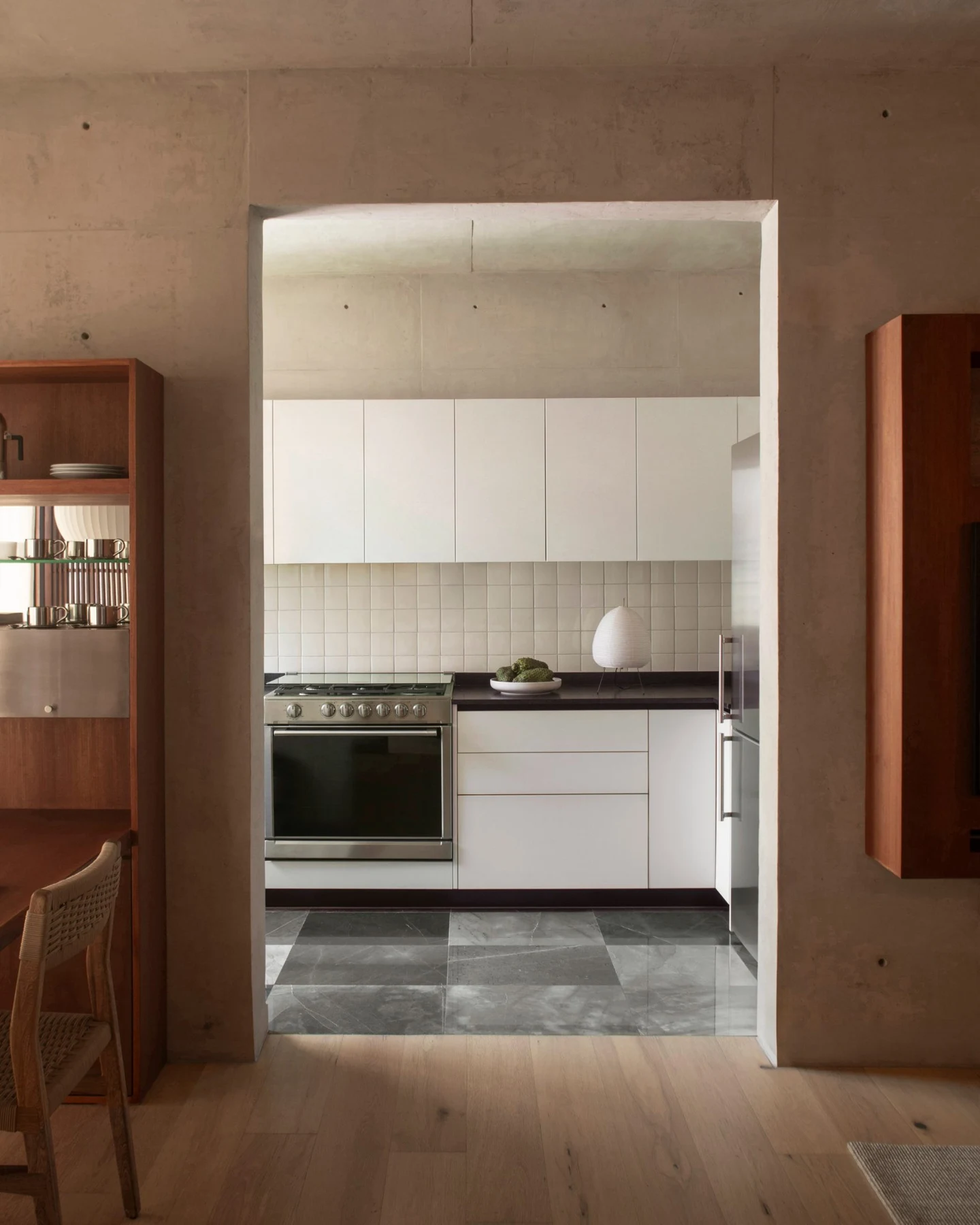 White kitchen with stainless-steel appliances framed by concrete walls and timber joinery
