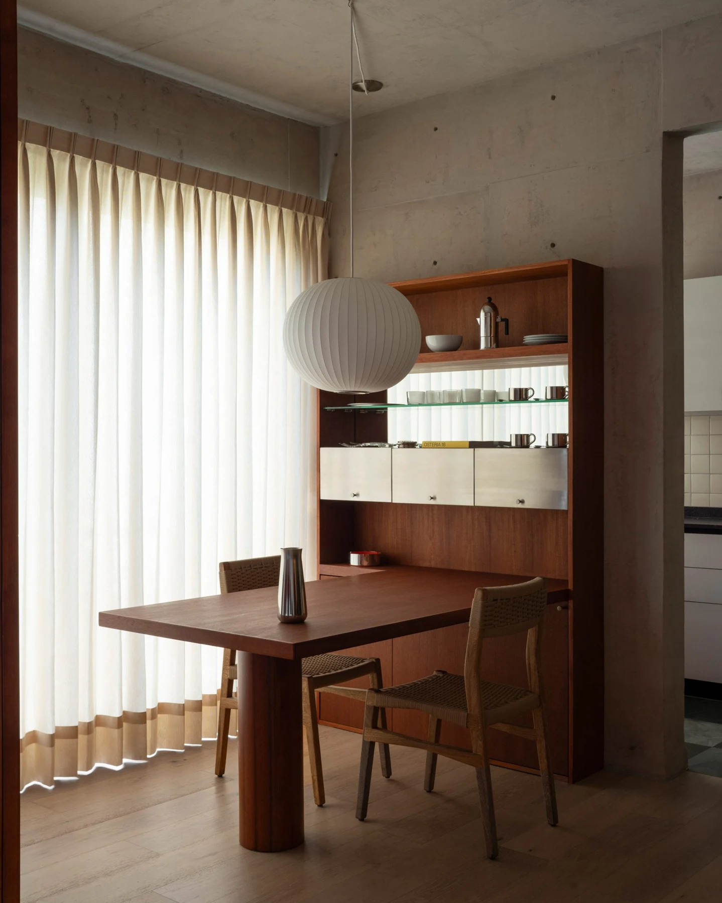 Timber dining table and shelving with reflective metal details beneath a concrete ceiling