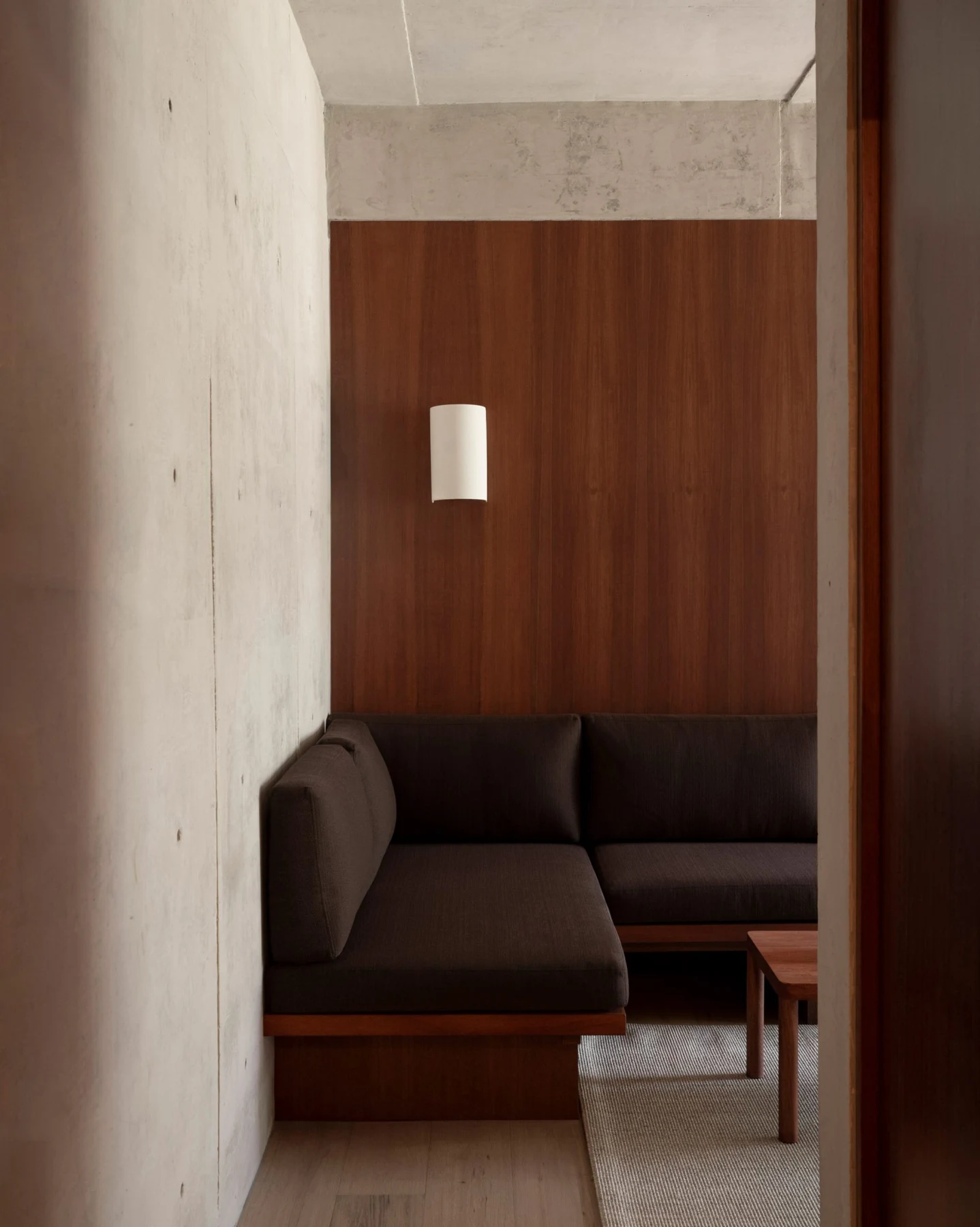 Dark built-in sofa against timber panelling and concrete walls, shown only for context