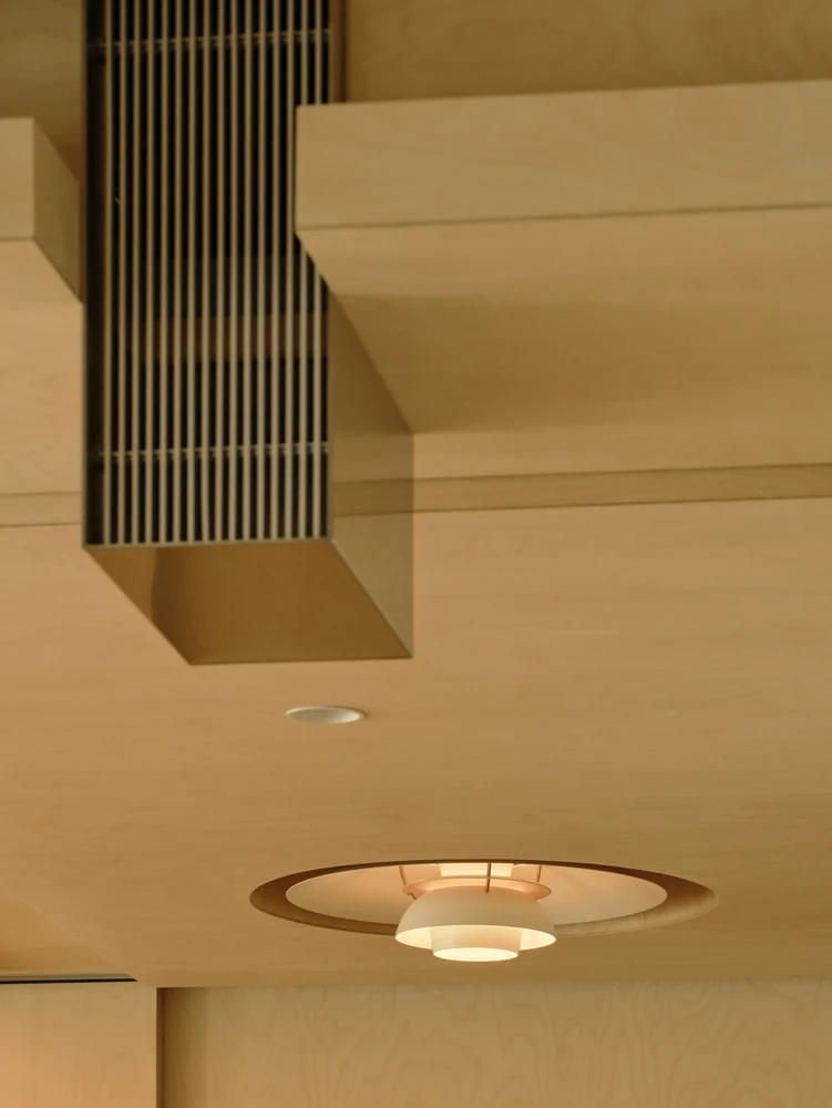 Vertical dark ventilation grille integrated into a projecting timber ceiling element