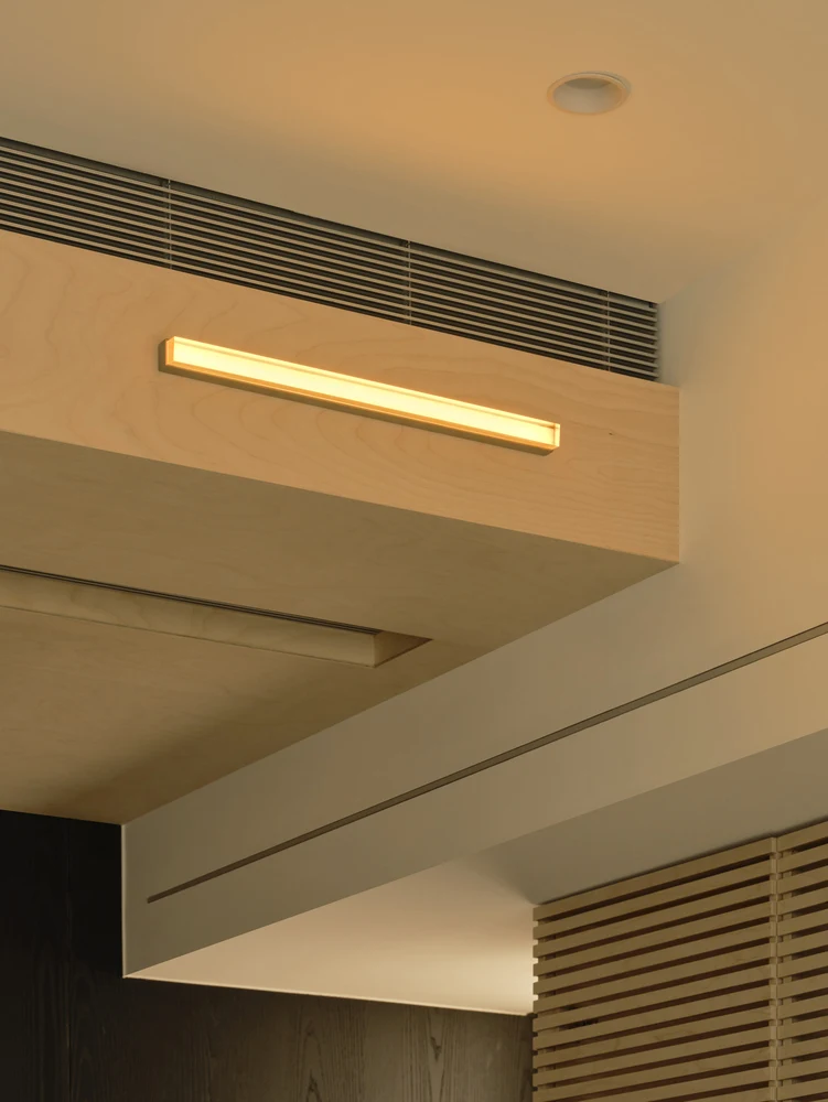 Long ventilation grille integrated above a timber ceiling volume, with a slim slot along the adjoining white bulkhead