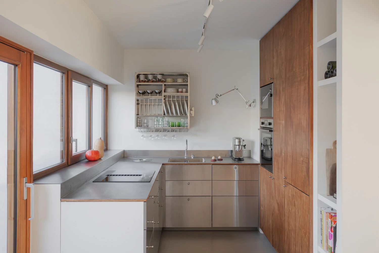 Metal kitchen worktops and drawers, neatly organised wall-mounted dish rack and articulated silver task lamp extending from the wall